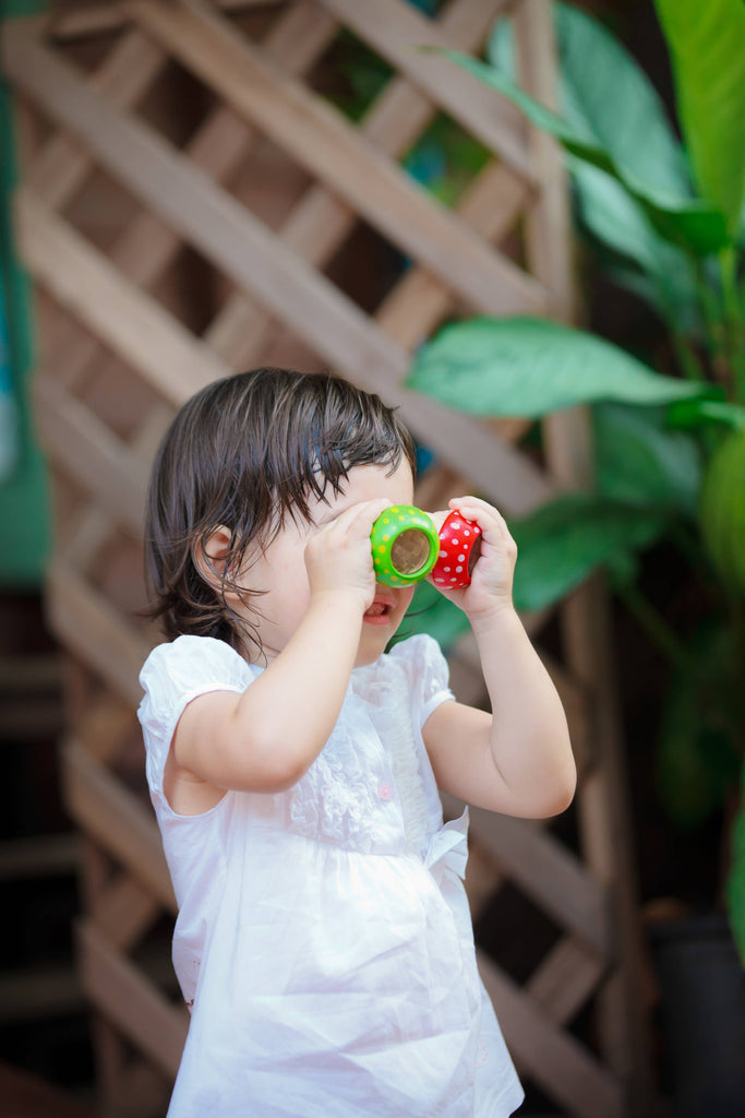 A young child looking through a pair of colorful PlanToys Mushroom Kaleidoscope binoculars outdoors, inspired to explore and develop creative thinking skills.