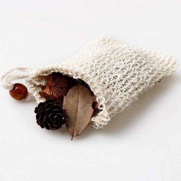 A small, eco-friendly Jungle Culture sisal soap bag made of natural fiber mesh lies on a flat surface, partially spilling its contents of a conifer cone, chestnut, dried leaf.