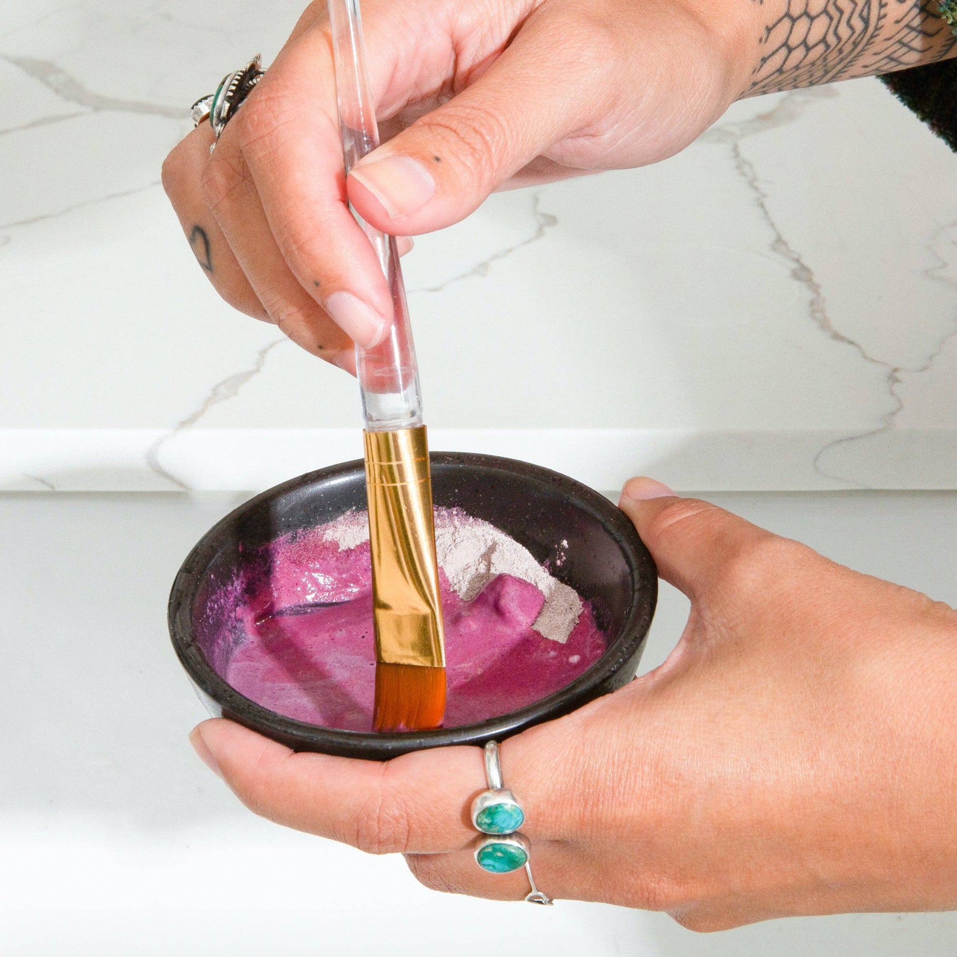 A person holding a bowl with Canary Clean Products - Bentonite Clay + Rose Face Mask and a brush, apparently preparing to color hair.