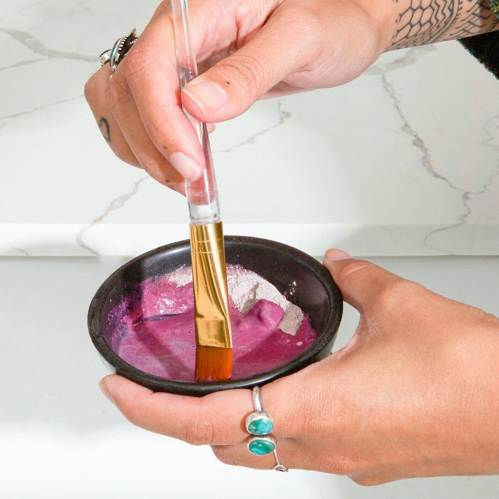 A person holding a bowl with Canary Clean Products - Bentonite Clay + Rose Face Mask and a brush, apparently preparing to color hair.