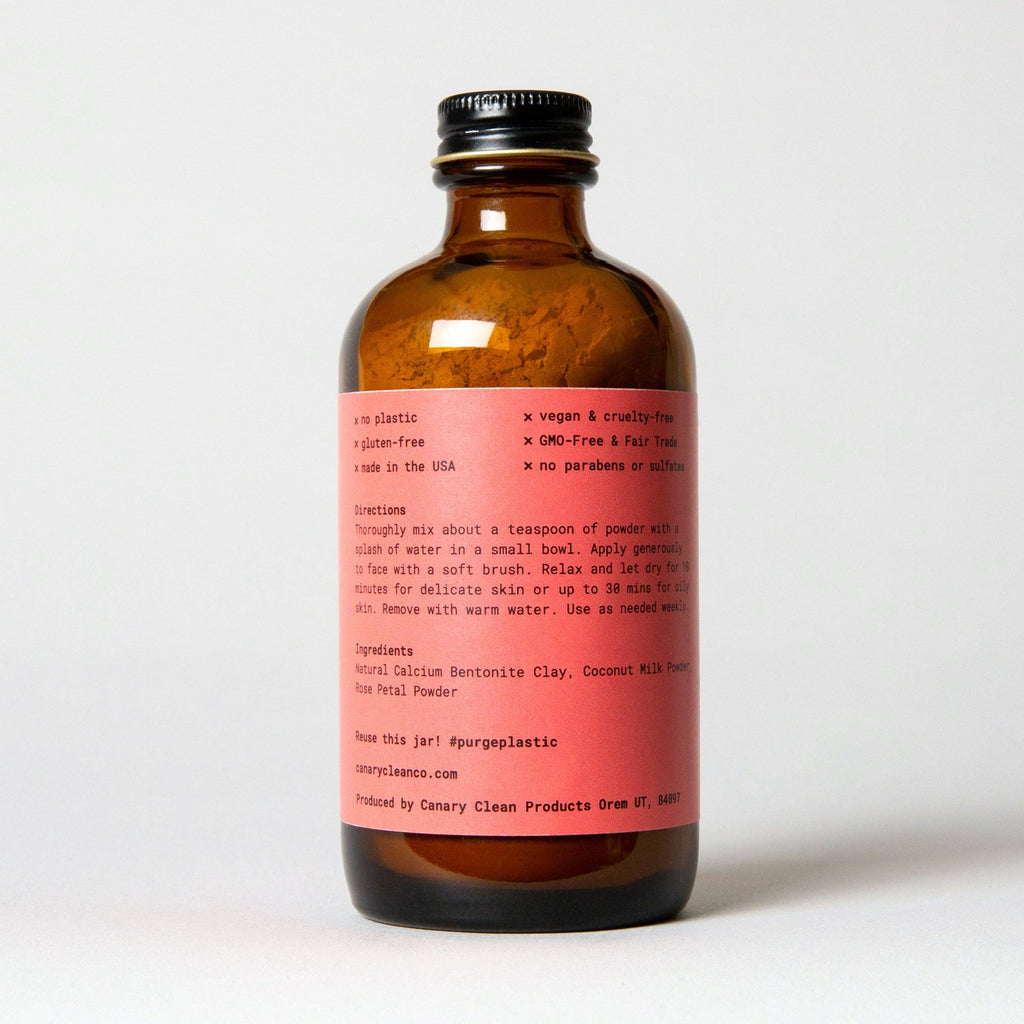 An amber glass bottle with a pink label detailing Canary Clean Products' Bentonite Clay + Rose Face Mask, featuring natural, vegan, and cruelty-free ingredients for skin rejuvenation, along with usage instructions.