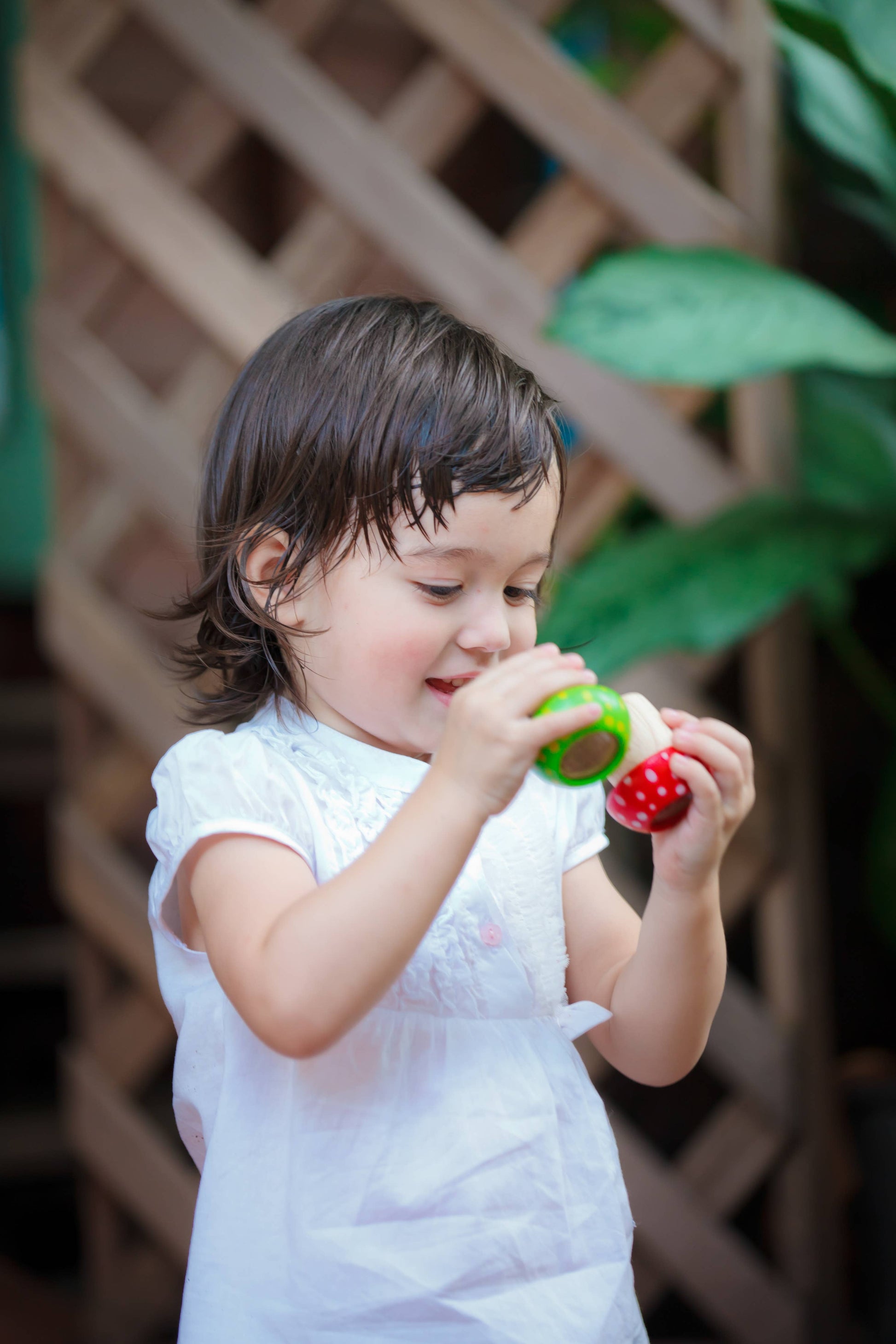 A young child is playing with a Mushroom Kaleidoscope from PlanToys outdoors, exploring their creative thinking skills.