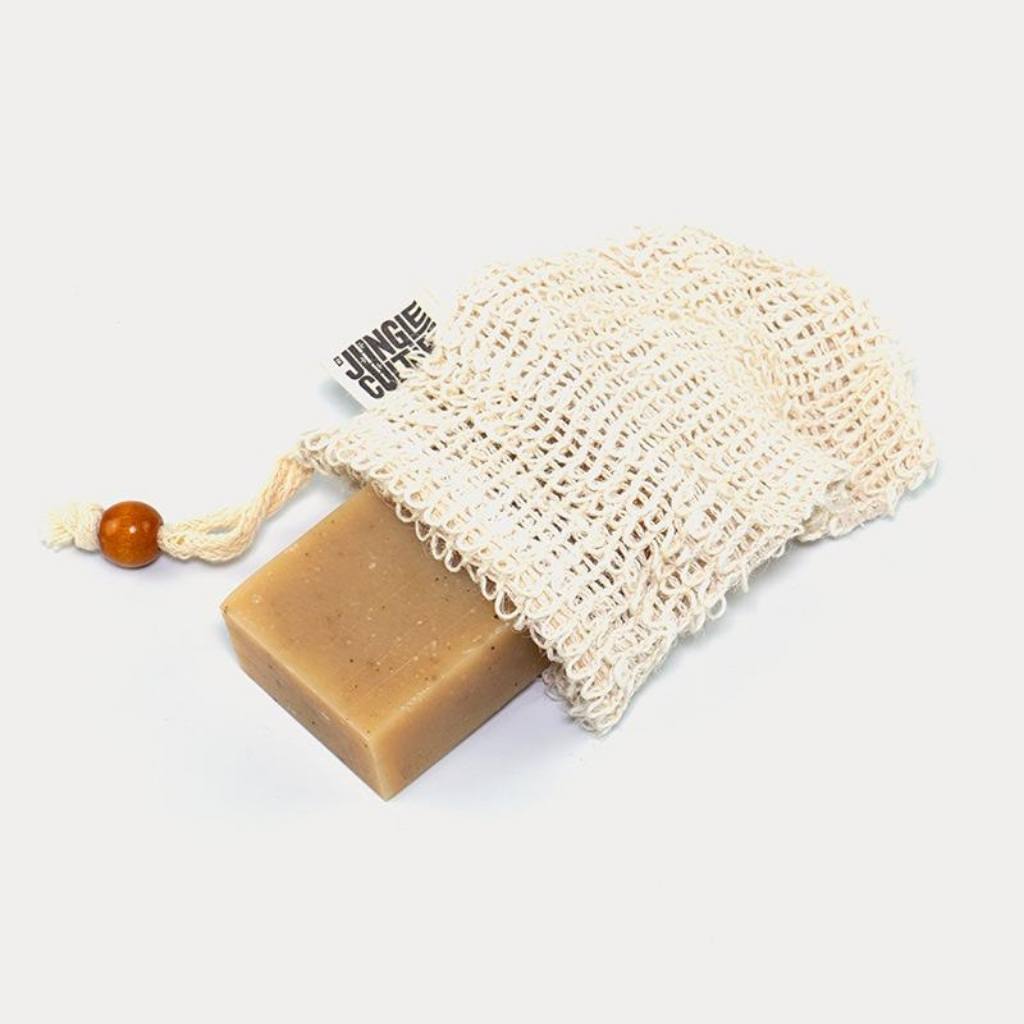 A bar of soap resting beside an empty Jungle Culture Sisal Soap Bag- Natural Fiber Mesh Soap Pouch Mesh on a white background.