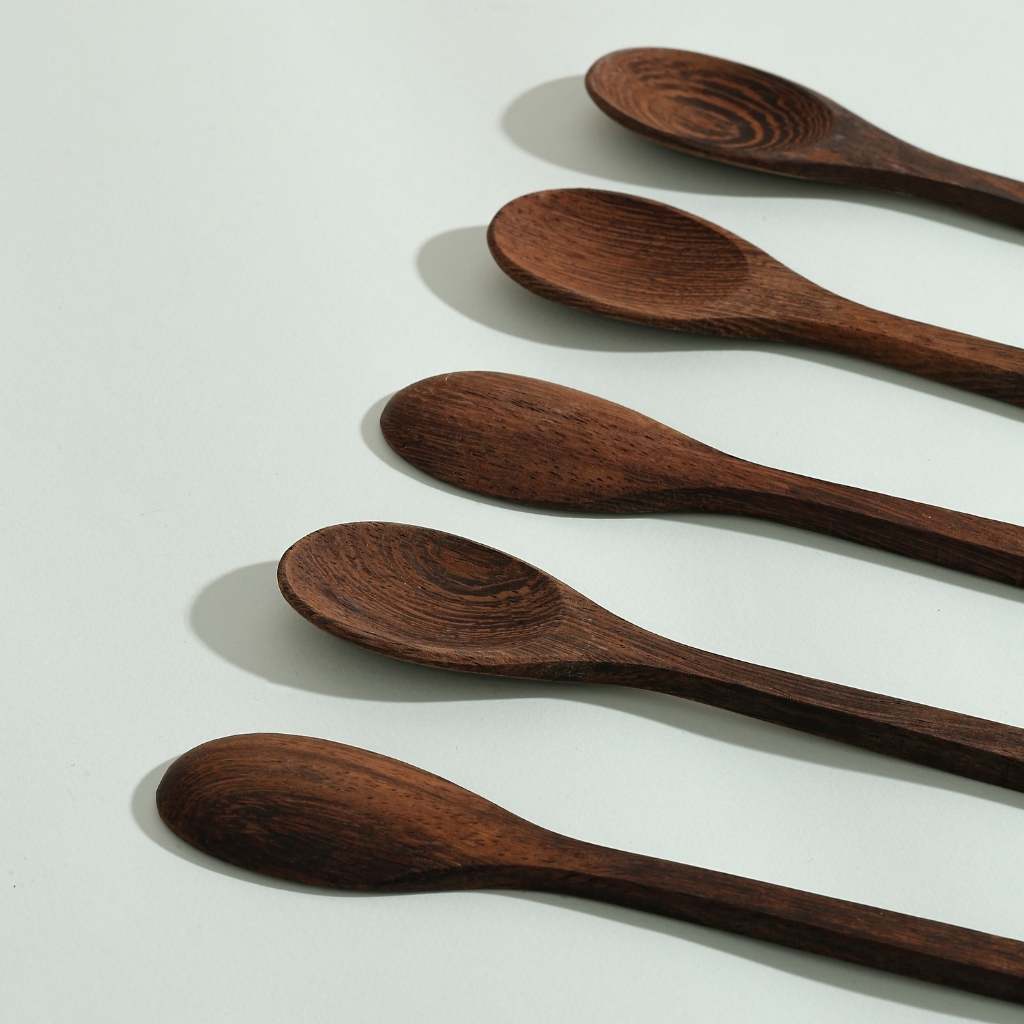 Four Jungle Culture Coconut Bowls Spoons of varying sizes arranged in a row on a pale surface with shadows indicating light coming from the top left corner.