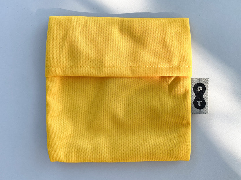 A folded yellow eco-PUL Pad Wrapper from Plum Thyme with a clothing size tag showing the number 8.