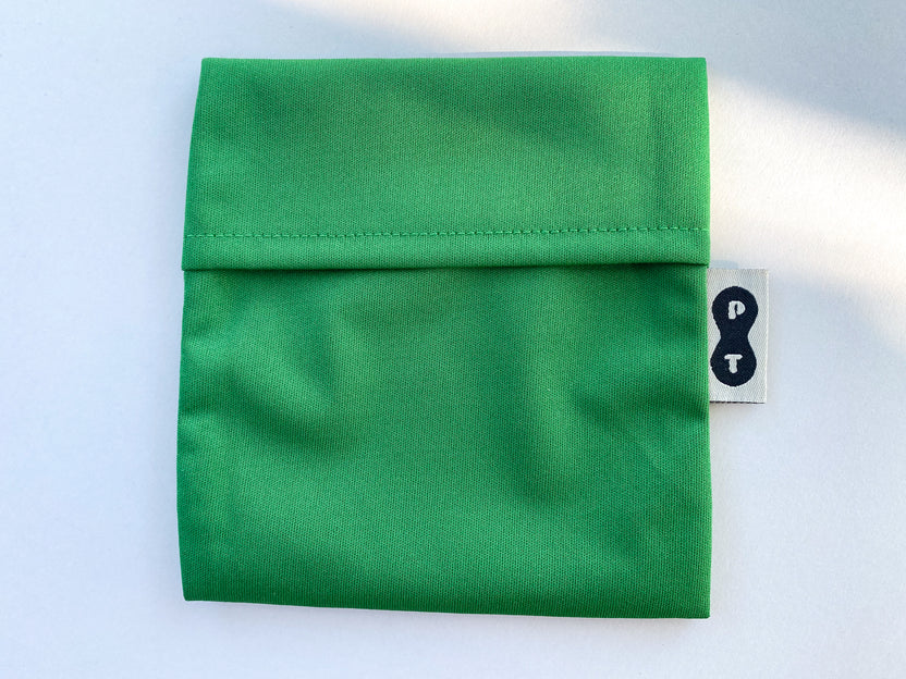 Folded green eco-PUL fabric with a visible seam and a black-and-white care instruction label for Plum Thyme's Pad Wrapper.