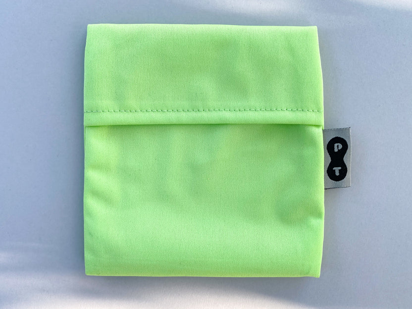 Neon green eco-PUL fabric folded neatly on a light surface with a small black and white Plum Thyme brand label on the side, designed for mess-free Plum Thyme pad wrapper use.