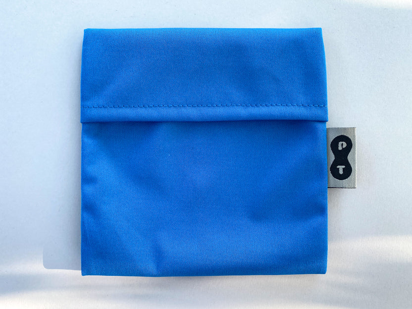 A folded blue eco-PUL fabric pouch with a visible Plum Thyme brand tag featuring a symbol or lettering on a light background, designed as a mess-free Pad Wrapper.