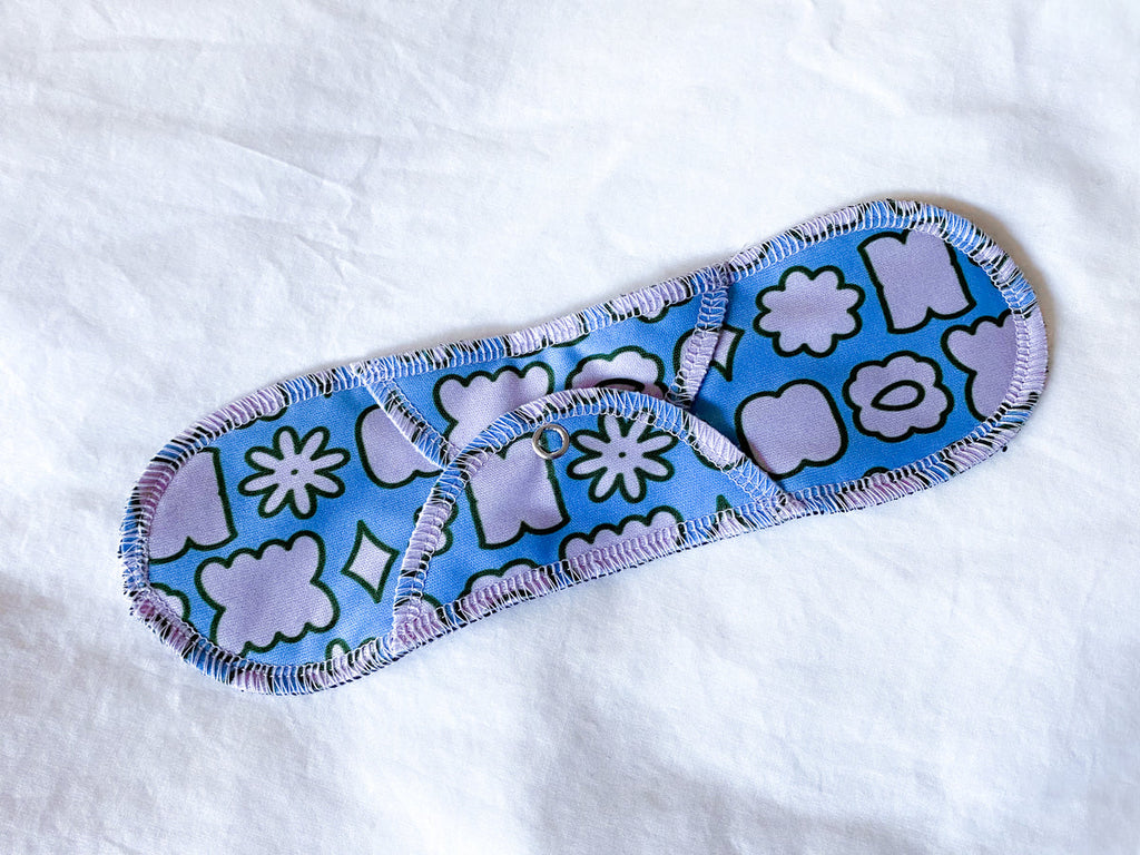 A Plum Thyme Moderate- Organic Reusable Menstrual Cloth Period Pad with a blue patterned design and enhanced absorbency laid out on a white surface.