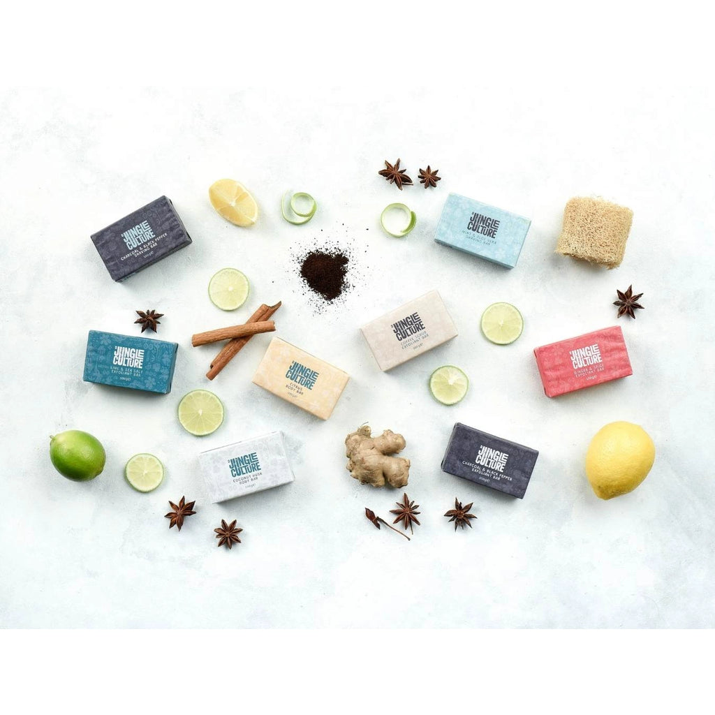 Assorted Jungle Culture handcrafted soaps arranged artistically with natural ingredients like lemon, lime, cinnamon, star anise, and a loofah surrounding them on a light background, including Jungle Culture coconut husk body soap.